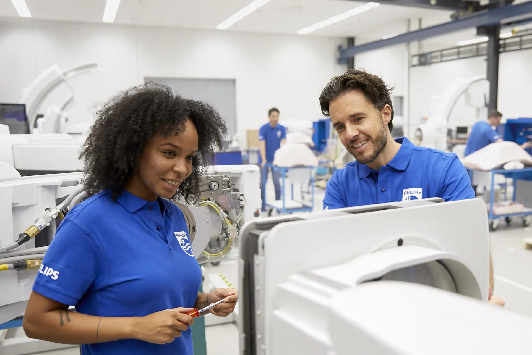 Black woman and white man wearing blue Philips polo shirts looking at a piece of medical equipment in a warehouse/laboratory environment