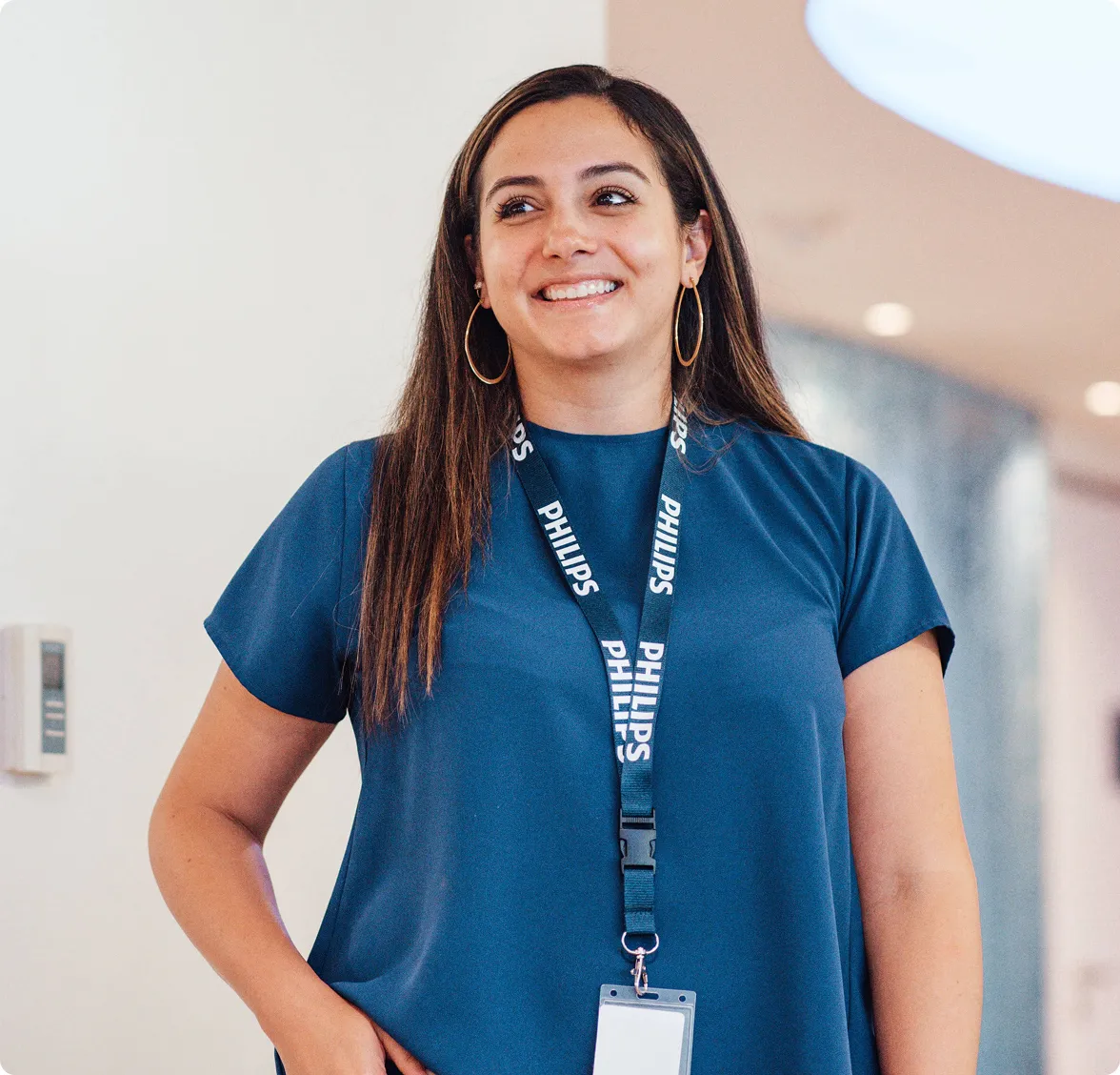 Young woman with long brown hair stood wearing a blue t-shirt and a Philips lanyard.