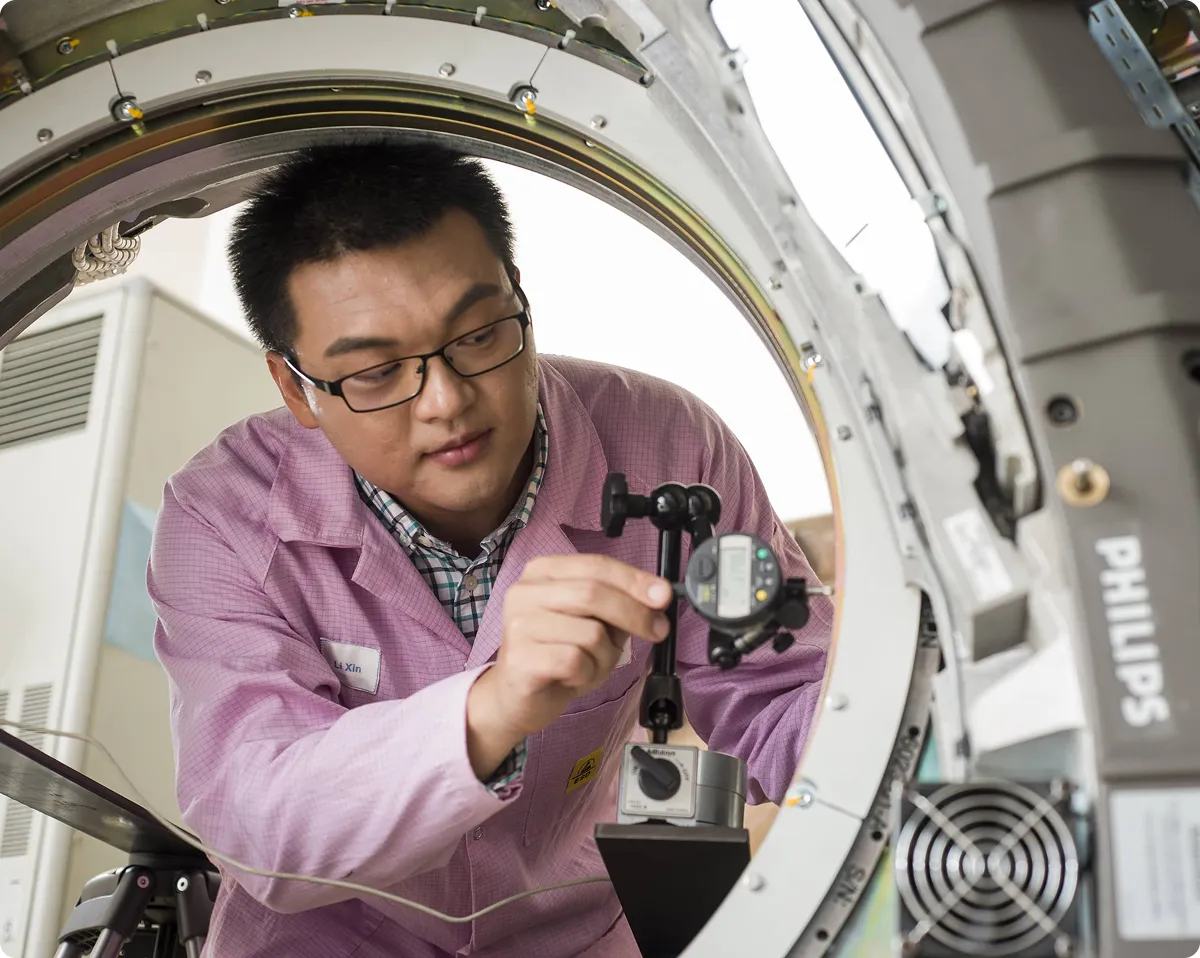 A male Philips technician wearing pink Philips overalls working on the construction of an MRI scanner.