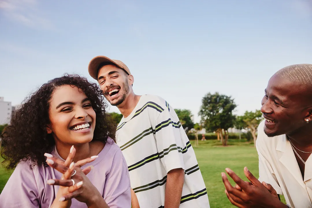 Young woman stood laughing with two male friends in a green park 