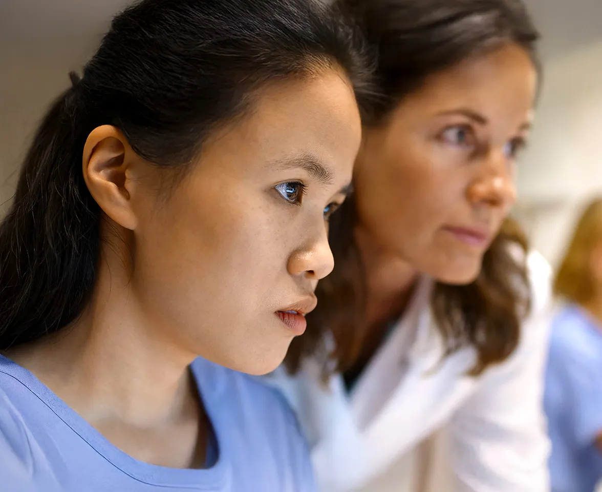 Closeup of a female nurse working at a computer with a senior female colleage looking over her shoulder.