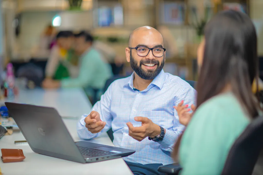 Smart bald man with glasses and laptop smiling and talking to female colleague in office