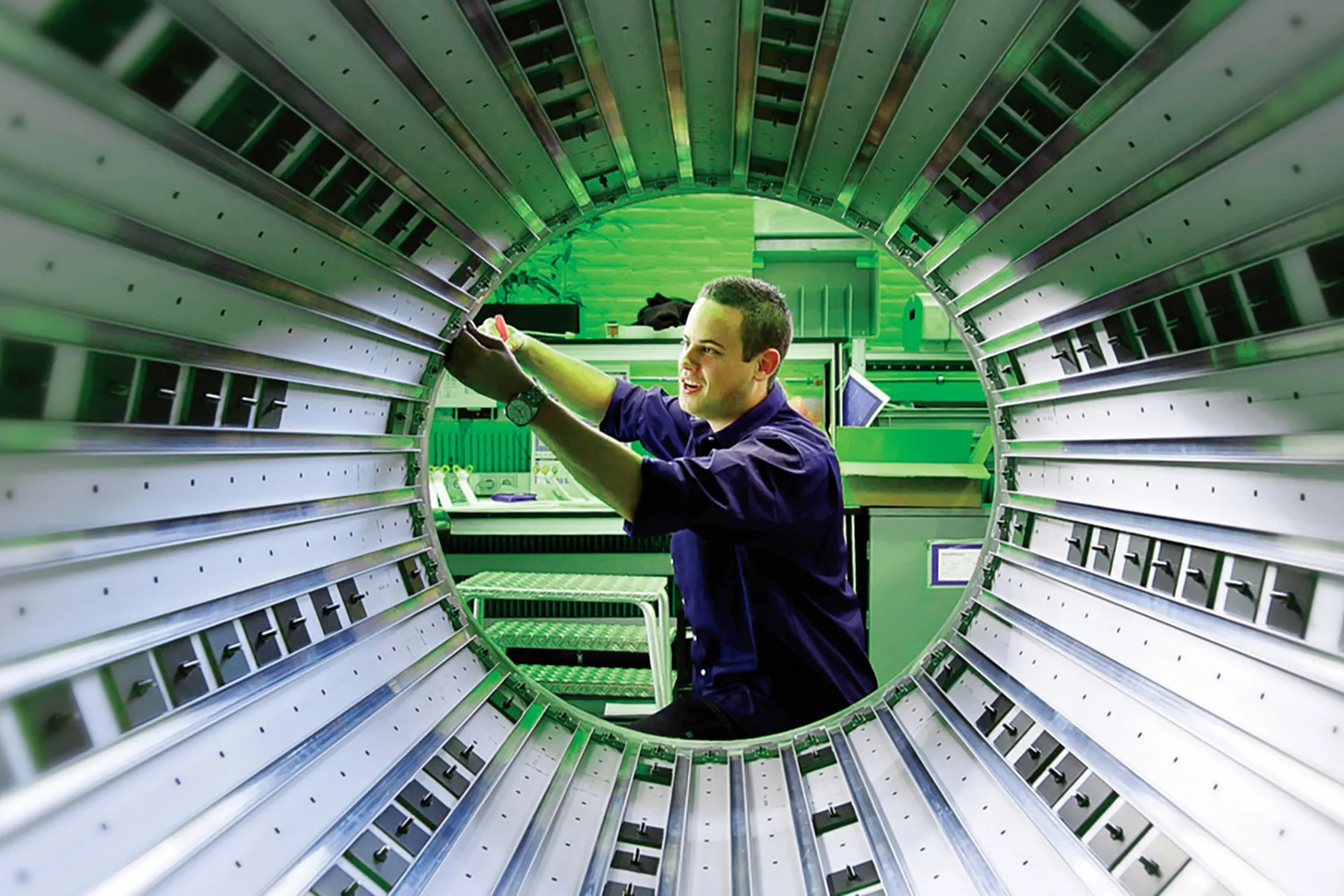 White male assembling parts of the internal cylinder of an MRI scanner in a warehouse environment