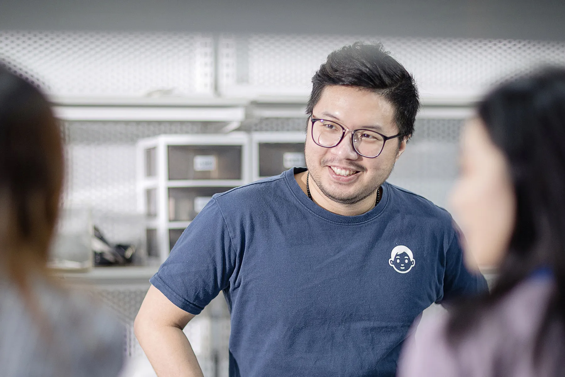 Asian man wearing a blue Philips t-shirt and glasses, smiling and conversing with colleagues